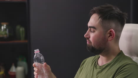 mann trinkwasser aus plastikflasche im büro