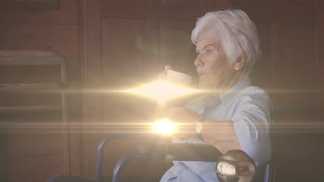 Animation-of-light-moving-over-senior-caucasian-woman-in-wheelchair-drinking-coffee
