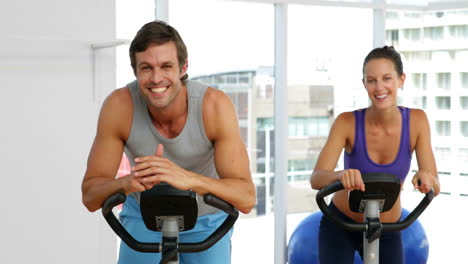 Fit-couple-exercising-on-bikes-in-fitness-studio