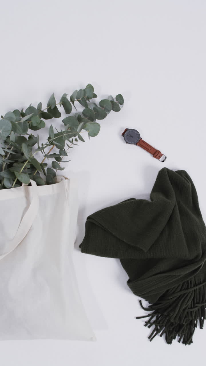 Vertical video of white canvas bag with plant, scarf, watch, copy space on white background