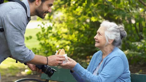 capturing joyful moments: a young man shares a delicious treat with an elderly woman in a serene park setting, celebrating connection through food and photography