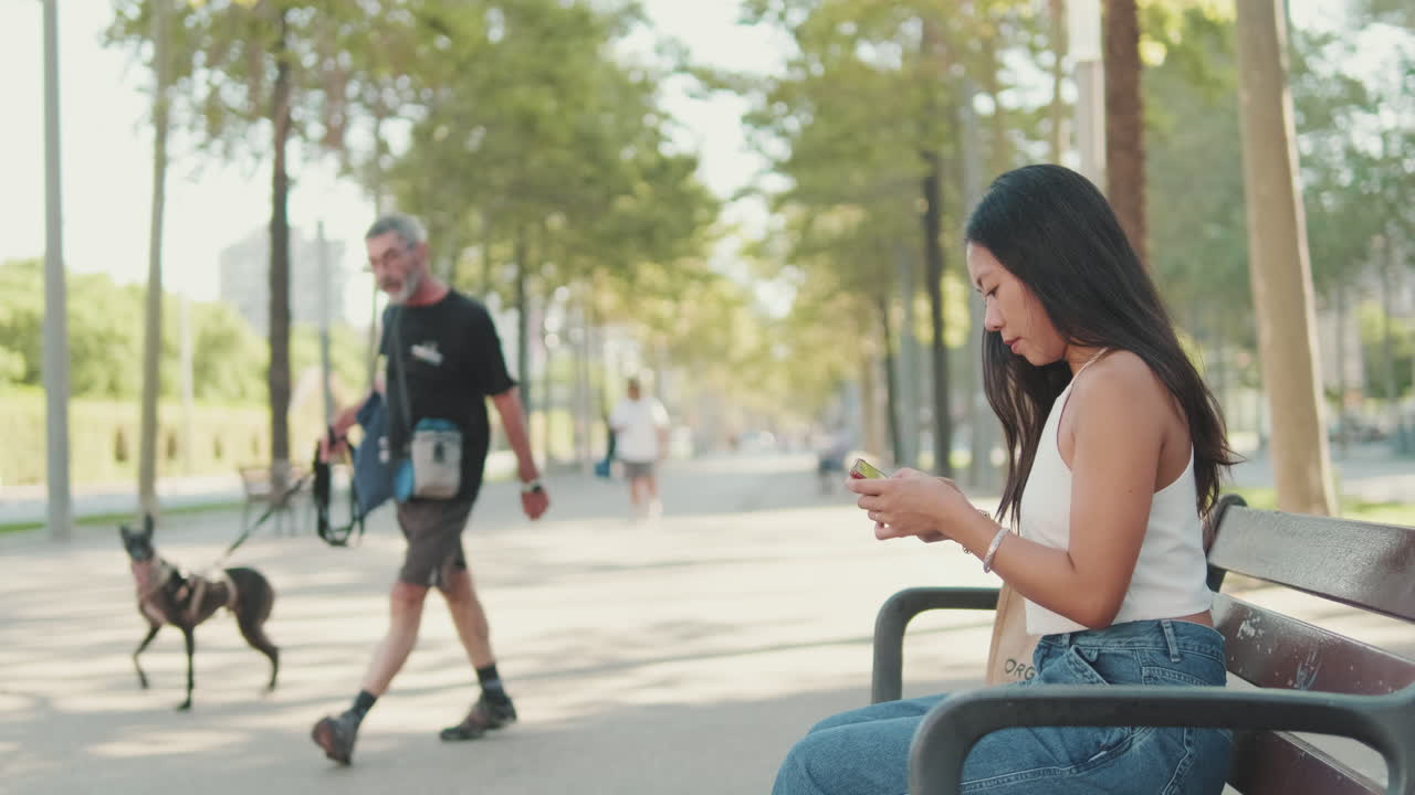 Kvinne som sitter på en benk i en park og bruker en smarttelefon