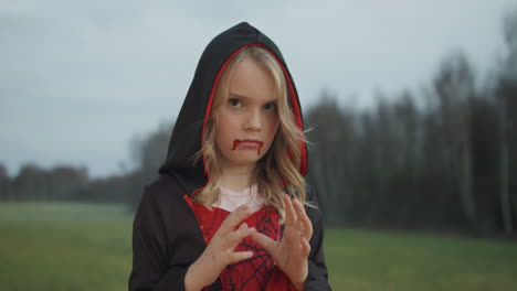 porträt eines kaukasischen jungen mädchens an halloween in einem vampirkostüm, wald im hintergrund