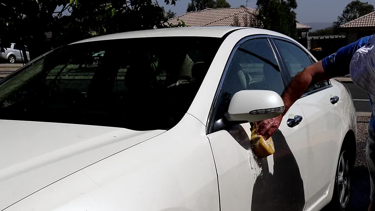 Man Washing a White Car in the Driveway