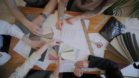 a collaborative design meeting in action, with team members selecting materials and colors, consulting floor plans, and engaging in creative decision-making for an interior design project.