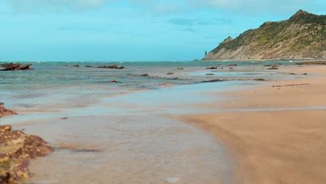 Eine-Fesselnde-Totalaufnahme-Fängt-Die-Malerische-Weite-Eines-Strandes-Ein,-Mit-Einem-Majestätischen-Leuchtturm,-Der-In-Der-Ferne-Emporragt-Und-Ein-Ruhiges-Küstenpanorama-Zeichnet