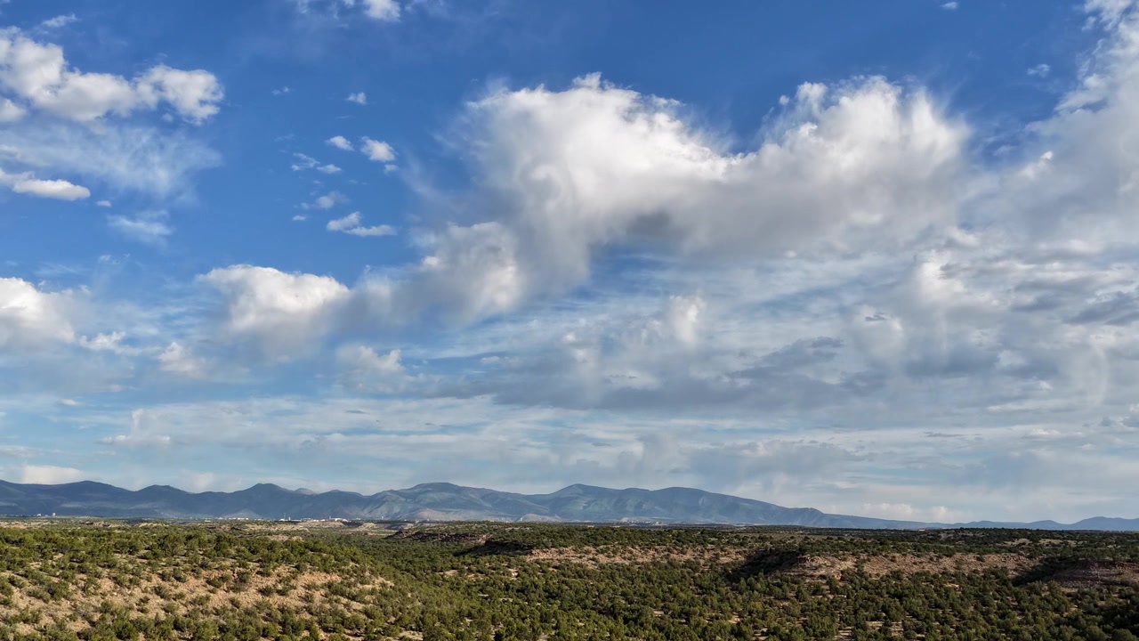 Un timelapse con drone che cattura nuvole in rapido movimento e una pioggerella leggera che si abbatte su un paesaggio del sud-ovest. Il tempo attivo si muove dinamicamente attraverso mesa aspre e una foresta di ginepri