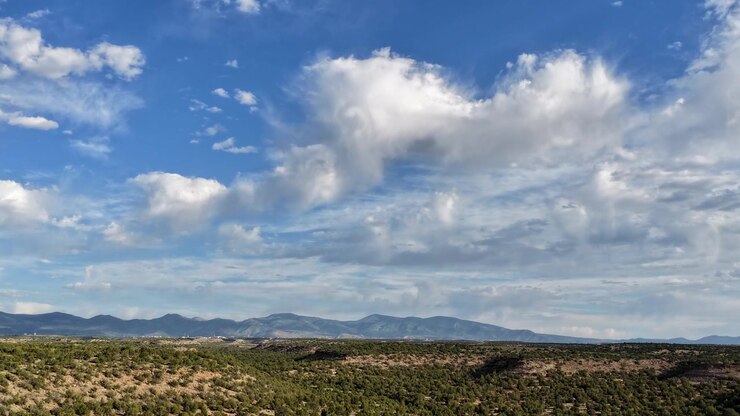 Un timelapse de dron que captura nubes de rápido movimiento y una llovizna ligera barriendo un paisaje del Suroeste. El clima activo se mueve dinámicamente a través de mesetas escarpadas y un bosque de enebros.