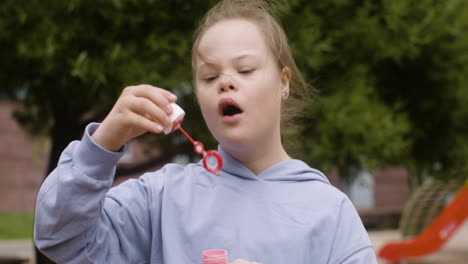 Nahaufnahme-Eines-Kleinen-Mädchens-Mit-Down-Syndrom,-Das-An-Einem-Windigen-Tag-Seifenblasen-Im-Park-Bläst