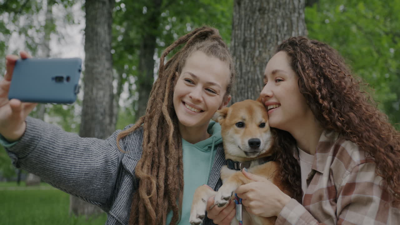 Two women taking a selfie with their dog in a park