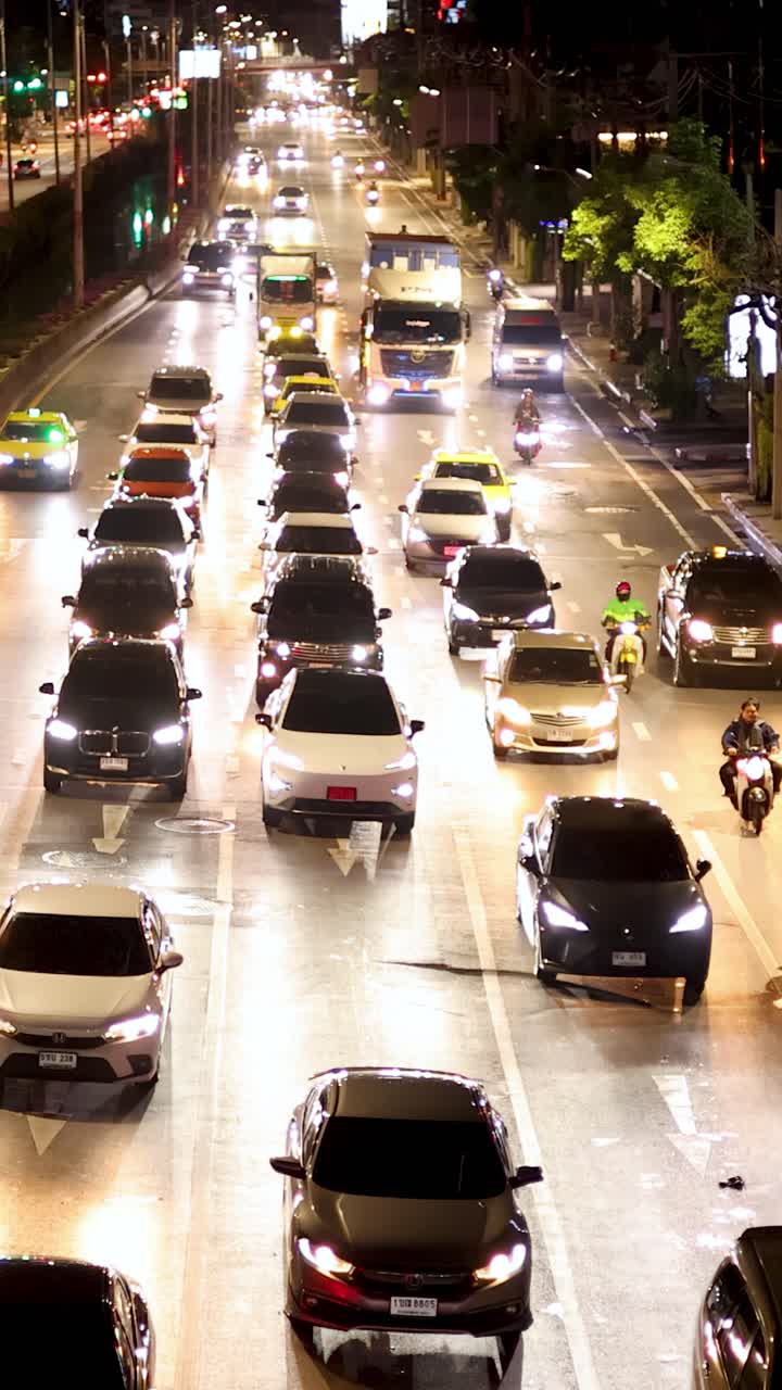 Strada urbana trafficata con auto, moto e taxi sotto i lampioni luminosi, vista dall'alto