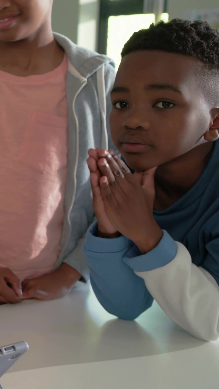 Vertical video: Gray console drawing kids to classroom table, boy in blue sweatshirt studying