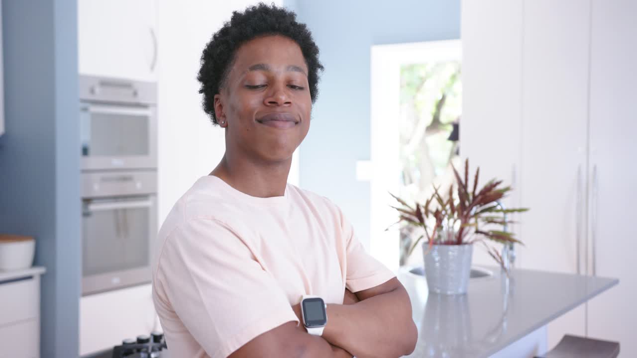 Uomo afroamericano che controlla lo smartwatch e un cavo, con le braccia incrociate, in posa, sorridendo alla fotocamera in cucina.