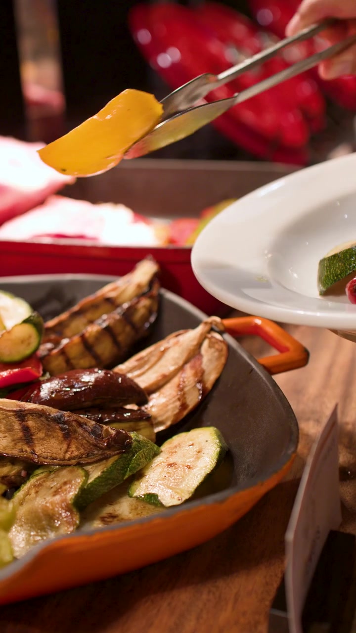 Primo piano di pinze di metallo che prendono verdure arrostite da un vassoio a un buffet di catering