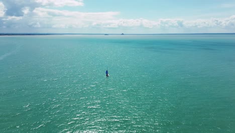 aerial view of a sailboat heading slowly toward mont saint-michel on a clear day. the wide shot shows the vast tidal bay