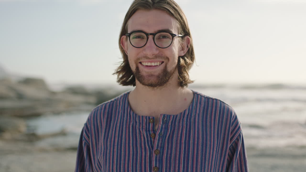 ritratto di un giovane con gli occhiali che sorride rilassato sulla spiaggia