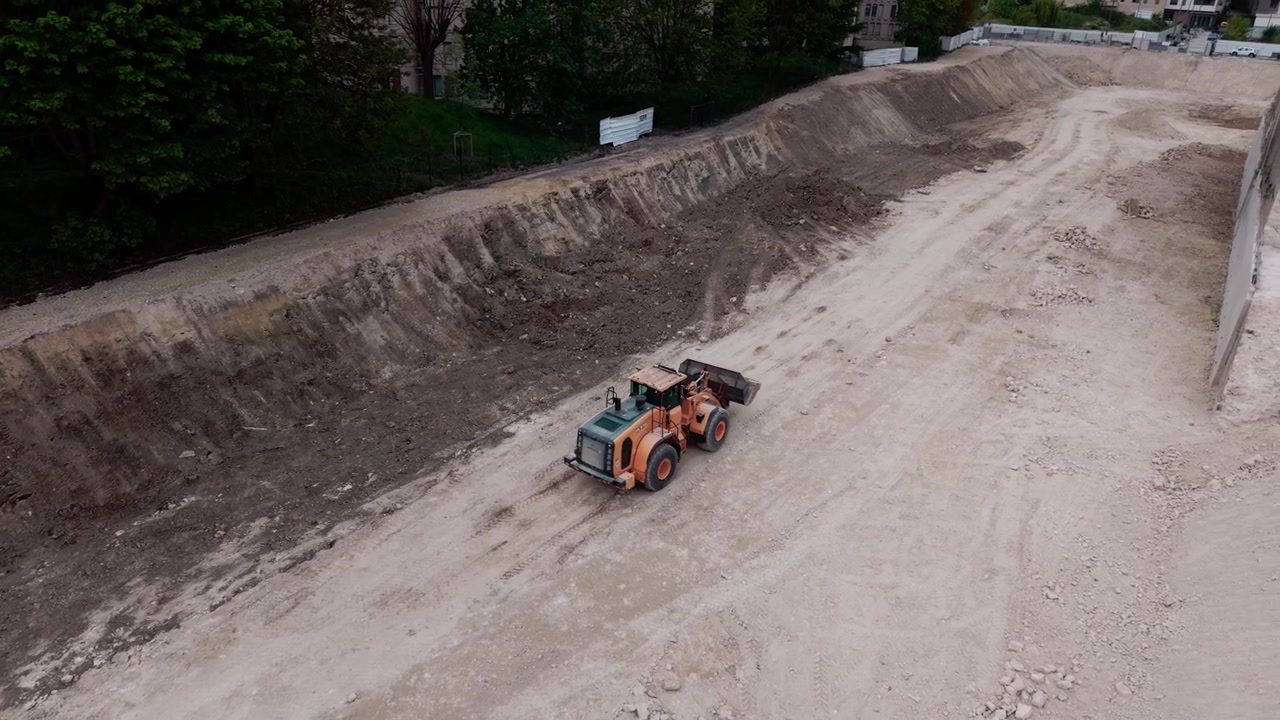 Wheel loader driving in large excavation pit for new building foundation in urban area