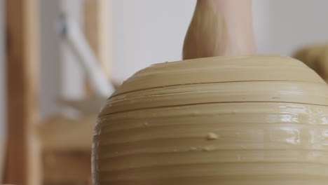 handheld close up shot of a female removing clay from a clay vase during pottery process, vase spinning on a potters wheel