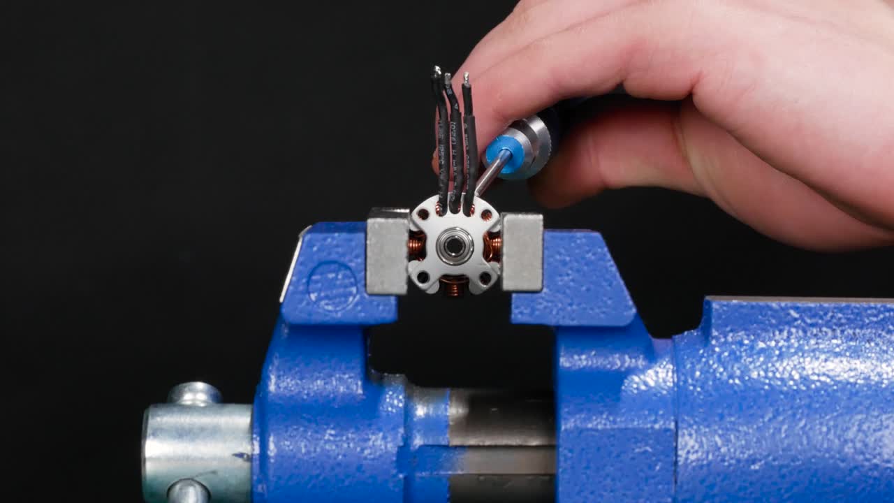 A man uses a screw driver and hammer to punch out a bearing that is installed into a motor that is being held by a vise on a work bench