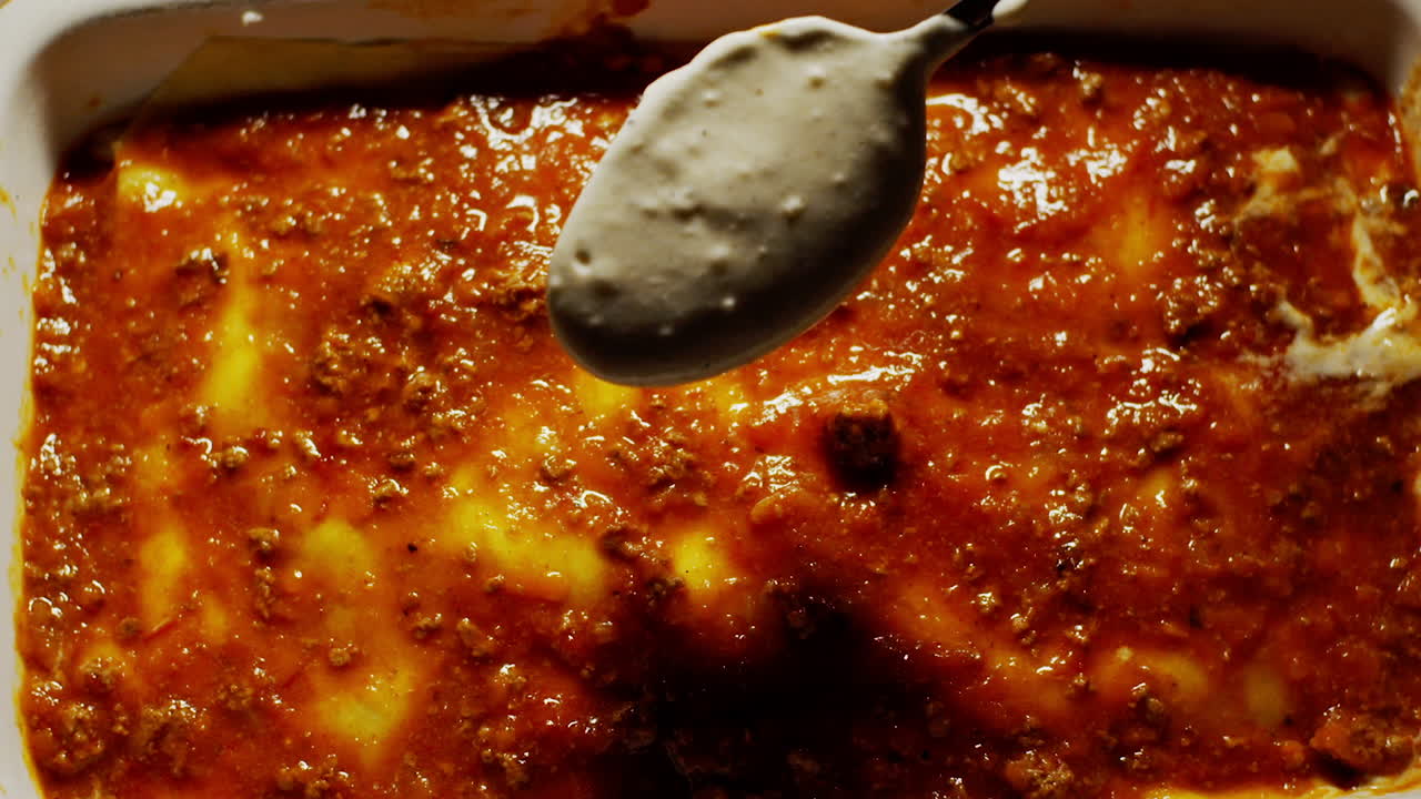 vista aérea de la salsa boloñesa y bechamel que se vierte en lasagana, de arriba hacia abajo