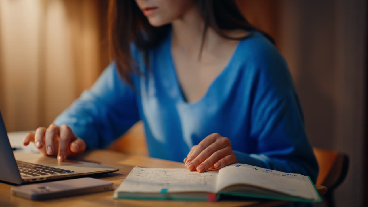 Busy lady working late looking laptop writing ideas in notebook at home closeup