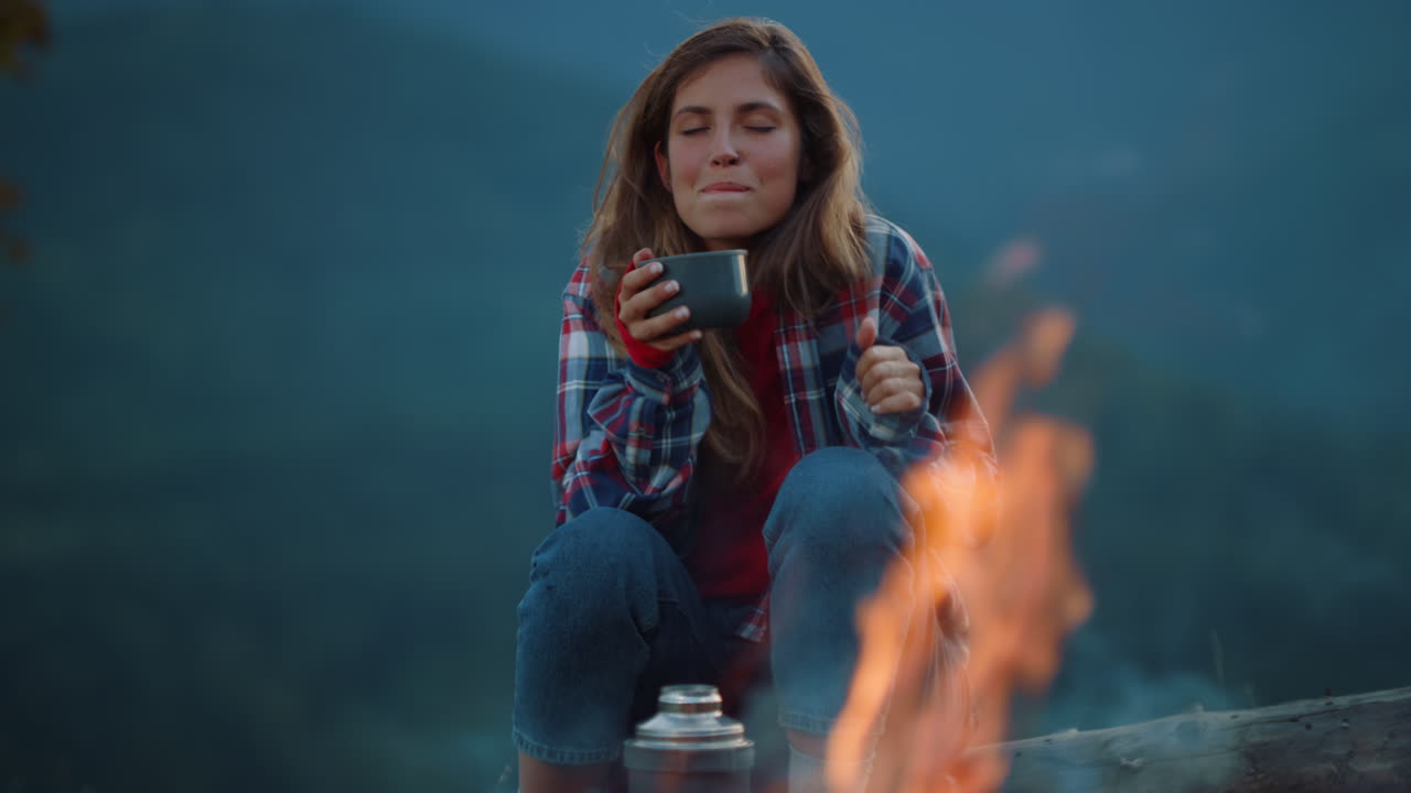 mujer bebiendo el té de la noche junto a la fogata. chill chica sueño en las montañas.