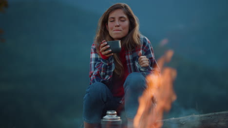 drinking woman enjoy evening tea by camping fire. chill girl dream in mountains.