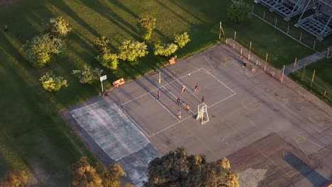 Aerial-flyover-asphalt-volleyball-field-and-friends-playing-game-during-sunset-light