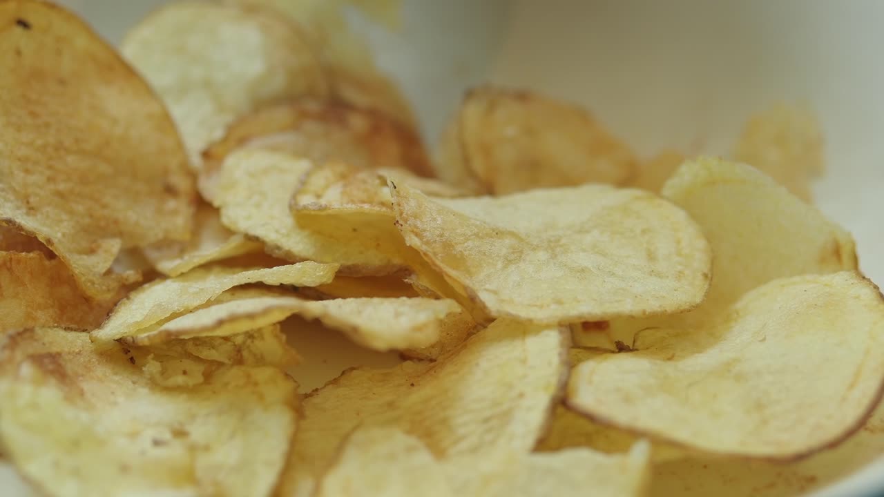 Close-up of Hand Picking Up a Crispy Potato Chip from a Bowl