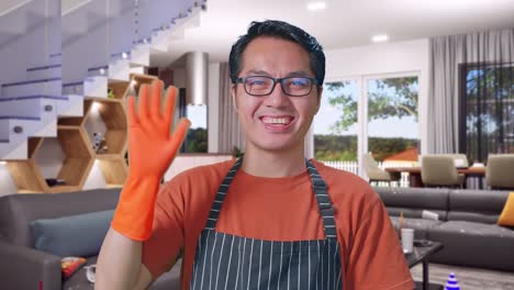 primer plano de una ama de casa asiática con un delantal agitando la mano y sonriendo mientras está de pie en la casa