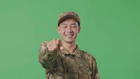 close up of asian man soldier smiling and touching his chest then pointing at you while standing in the green screen background studio
