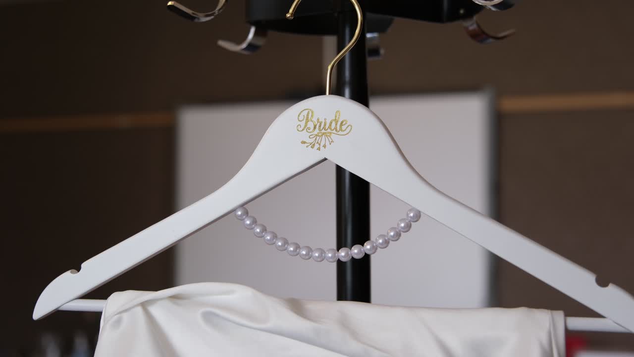 Tight shot of a Bride hanger adorned with pearls holding a white wedding dress. Elegant, intimate detail symbolising love, anticipation, and the beauty of bridal preparation