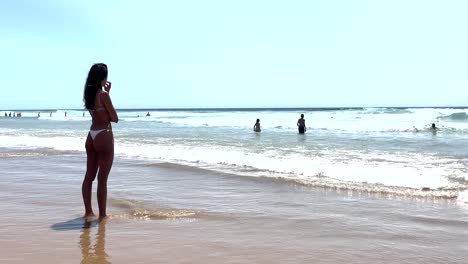 fit woman in a summer bikini is looking at the ocean with her feet in the water