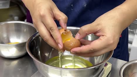 delicioso postre en preparación, pastelero rompiendo huevo, separando clara de huevo y yema de huevo en diferentes tazones de mezcla de acero inoxidable, ambiente de restaurante comercial