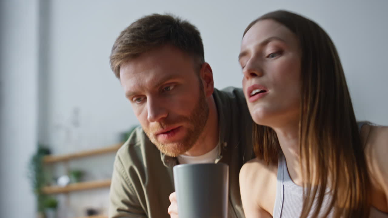 Lovely pair drinking coffee looking laptop in kitchen closeup. Happy man woman