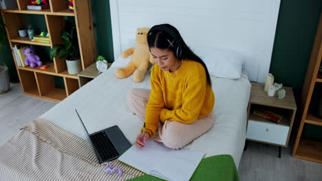 woman studying with laptop and headphones on bed