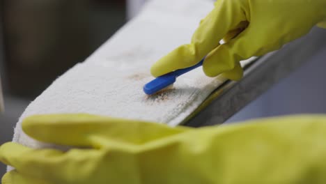 hands in gloves removing stain on white towel using toothbrush