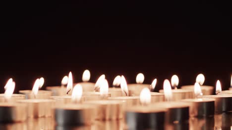 video of rows of tea candles with white flames and copy space on black background