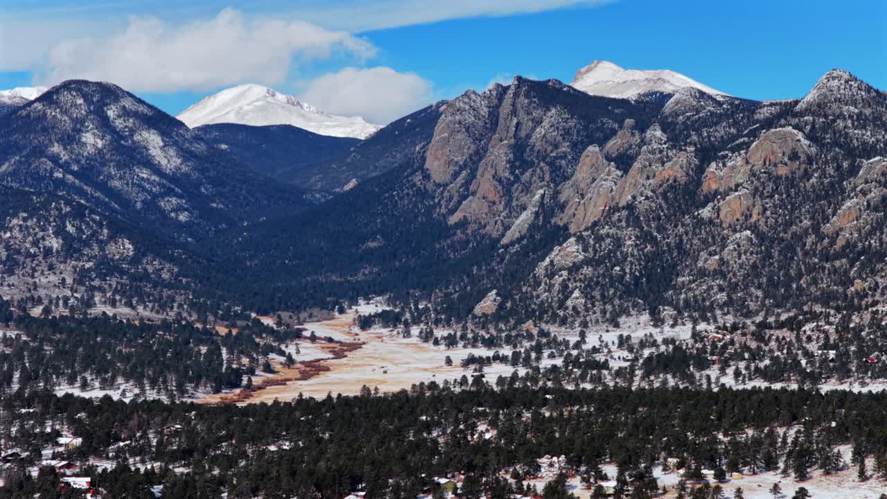 Estes Park, città di montagna nel Parco Nazionale delle Montagne Rocciose, Colorado. Formazione rocciosa Lumpy Ridge Twin Owls, Catena del Mummy Range. Paesaggio della valle ripreso con drone aereo, tramonto, neve fresca, nuvole, cielo azzurro, soleggiato. Panoramica in avanti e verso l'alto.