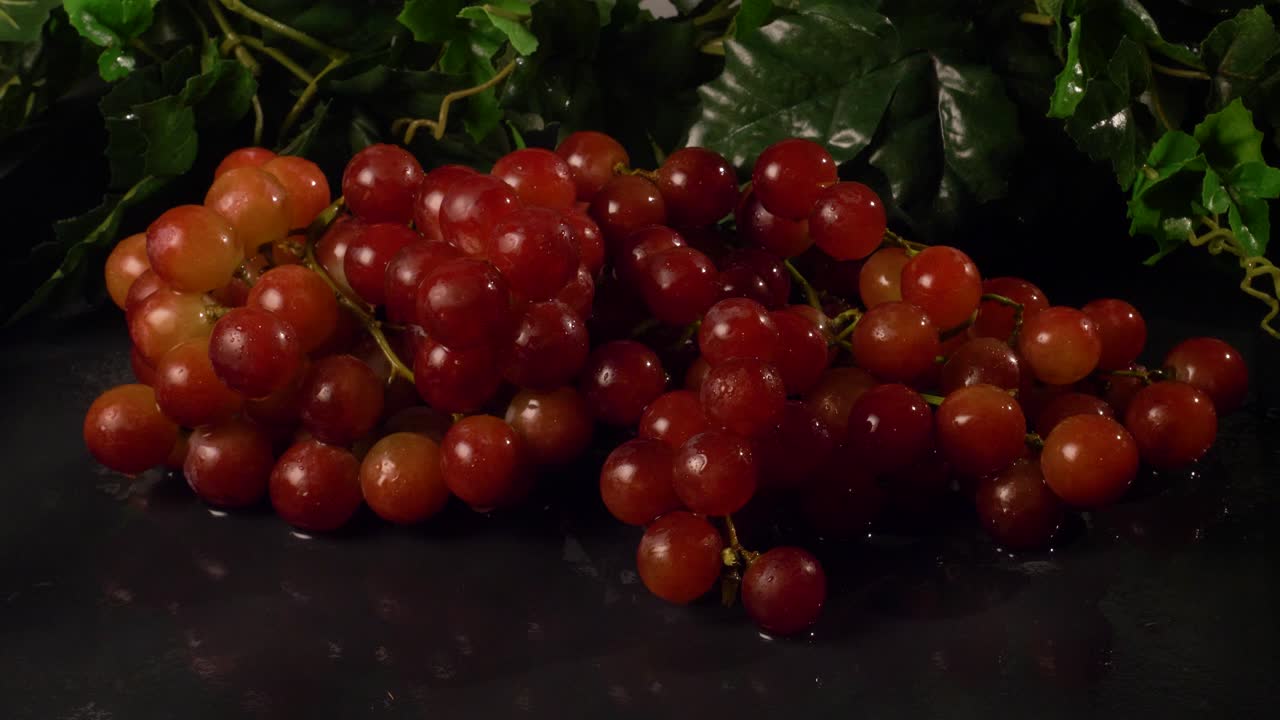 Seedless red grapes on a wet, black surface