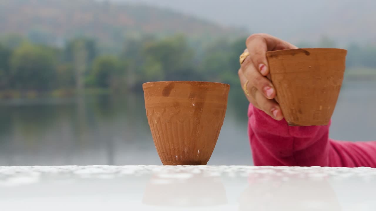 niña disfrutando de té caliente servido en una taza de arcilla de cerámica tradicional con el paisaje borroso del lago de montaña