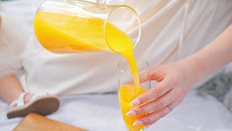 a mom is pouring orange juice during a picnic outside in a park