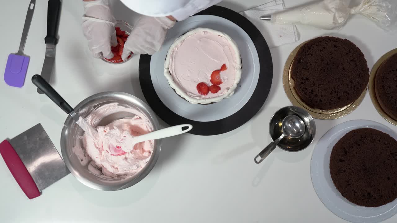 요리사는 이미 위에 크림이 있는 케이크 층에 잘라진 딸기를 놓고 있습니다.