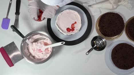 chef placing sliced strawberries on layer of cake that already has some cream on top.