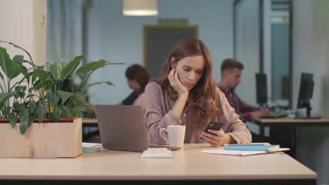 Müde-Frau-Scrollt-Beim-Coworking-Mit-Dem-Handy.-Porträt-Einer-Dame,-Die-Am-Telefon-Chattet