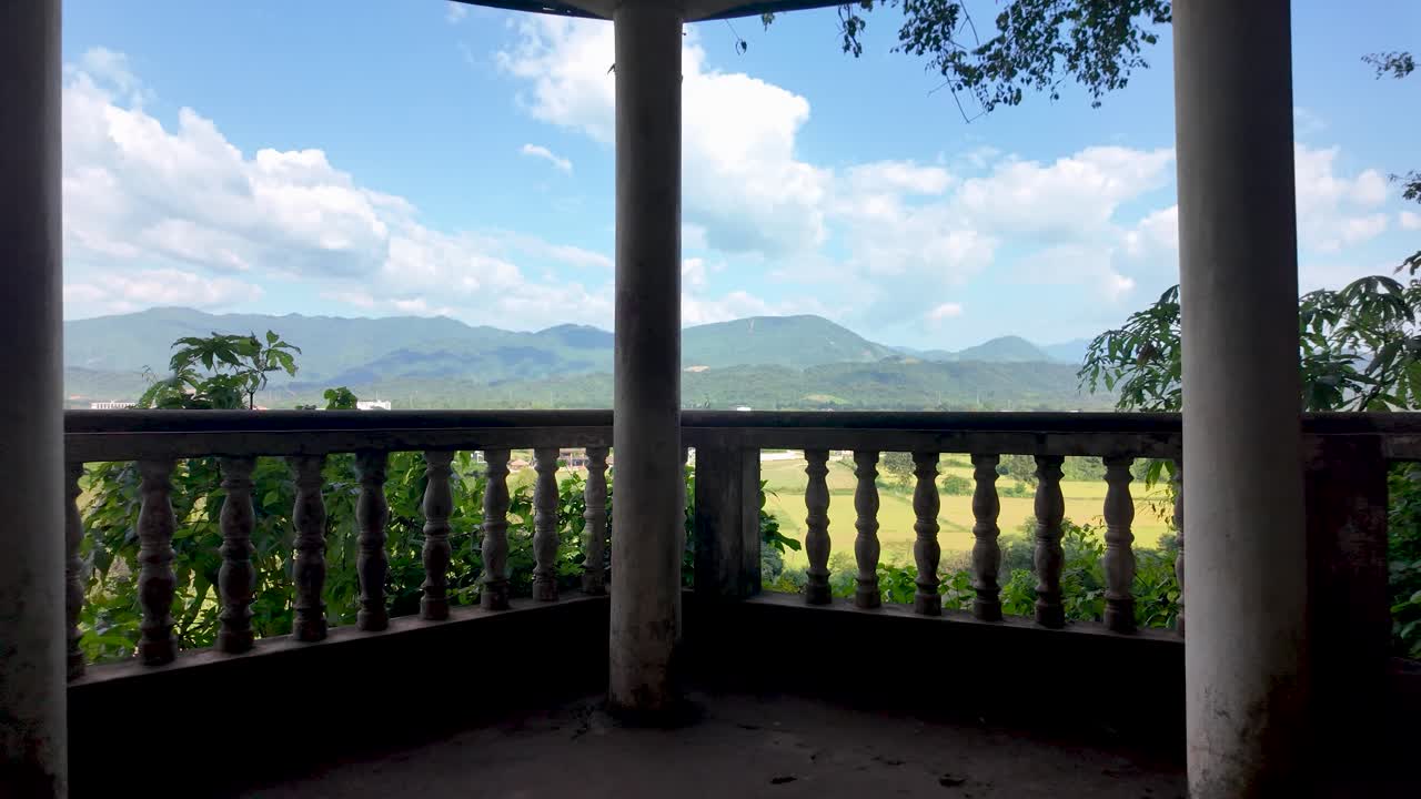 Vista de un balcón con montañas, río y campos verdes bajo un cielo azul. Avance con la toma