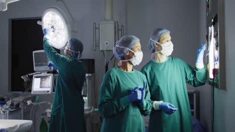 Video-of-two-diverse-female-surgeons-discussing-x-ray-on-lightbox-in-operating-theatre,-copy-space