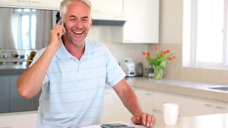 Happy-man-working-out-finances-at-the-counter-talking-on-the-phone