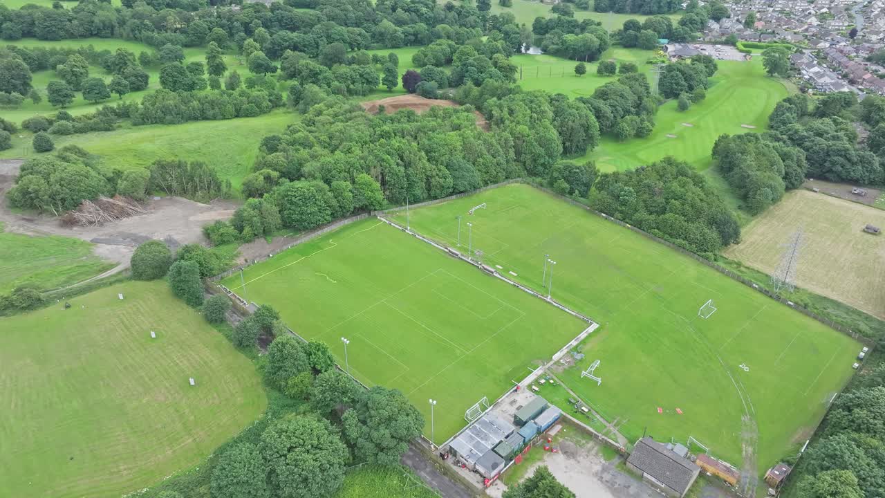 An aerial shot captures a sports field's vibrant green with goalposts and the dense foliage that encircles it. The contrast between the playing area and the vegetation creates a picturesque setting.