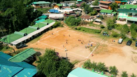 4k cinematic sport aerial drone footage of children playing on a footbal field in the mountain village of doi pui next to chiang mai, thailand on a sunny day